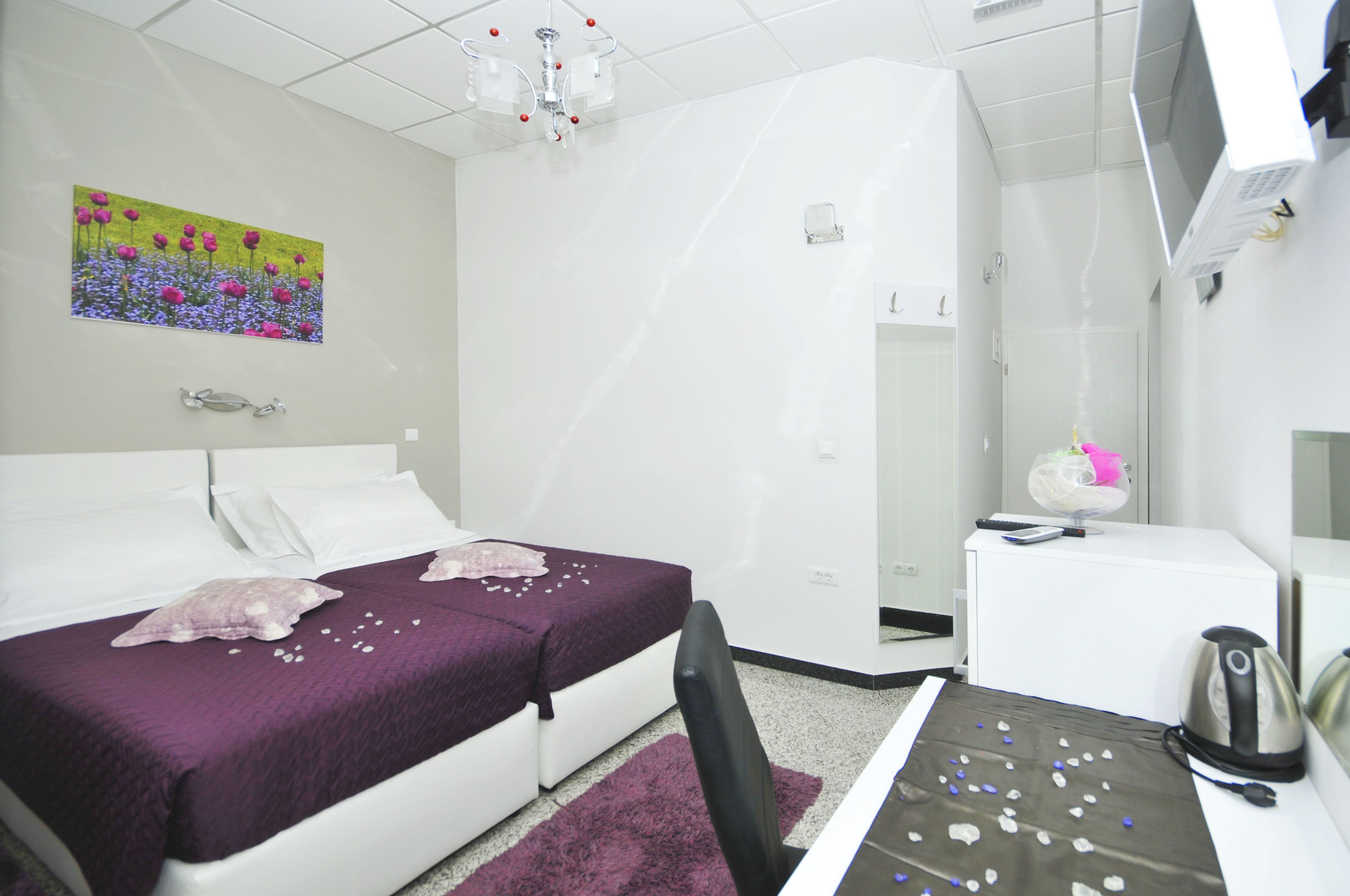 Habitación de hotel con cama, escritorio, silla, hervidor de agua y un cuadro en la pared.