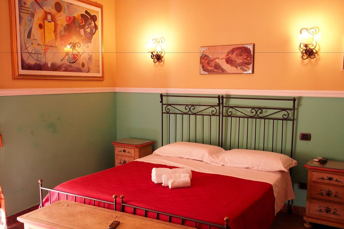 A room with a bed, a nightstand, a dresser, and wall-mounted light fixtures.