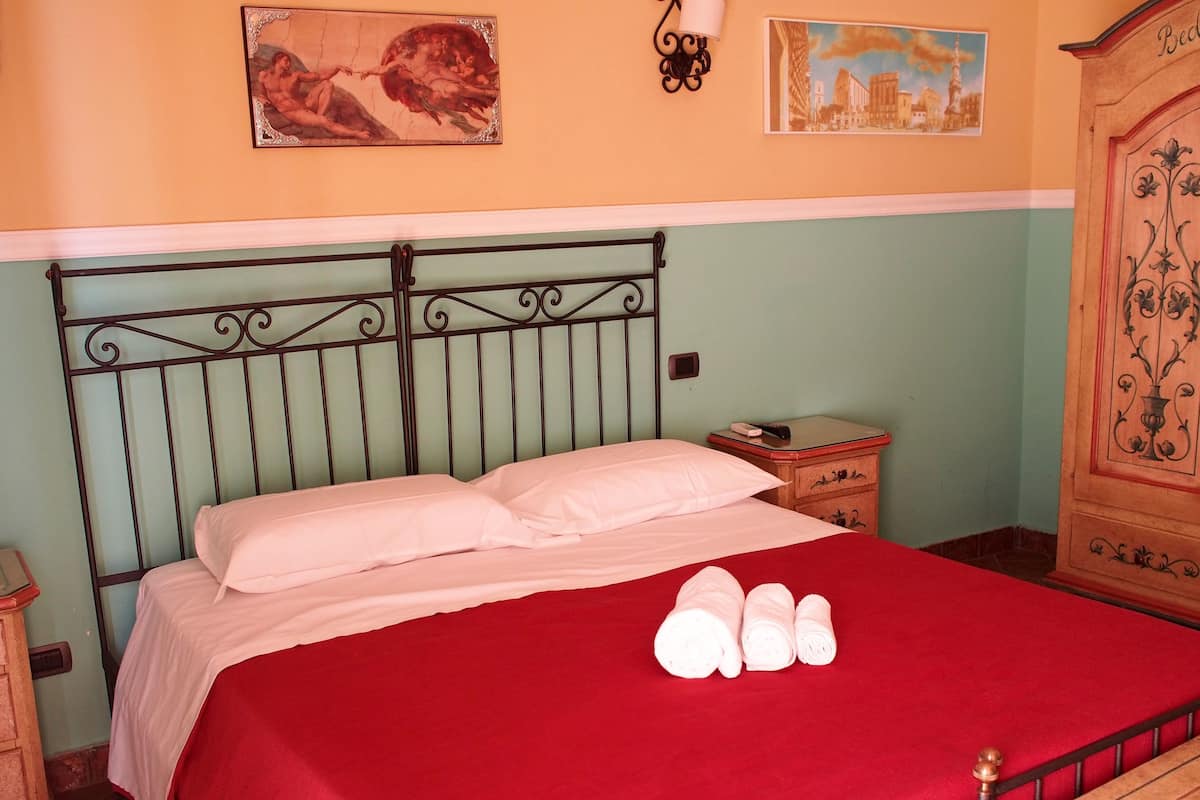 A bed with a red bedspread and white pillows, a nightstand with a lamp, and a wall with two framed pictures.