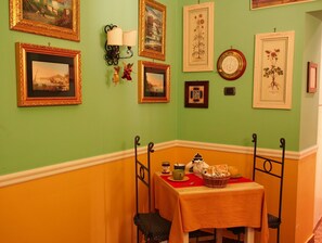 Une pièce aux murs verts, une table recouverte d’une nappe rouge et divers tableaux encadrés accrochés au mur.