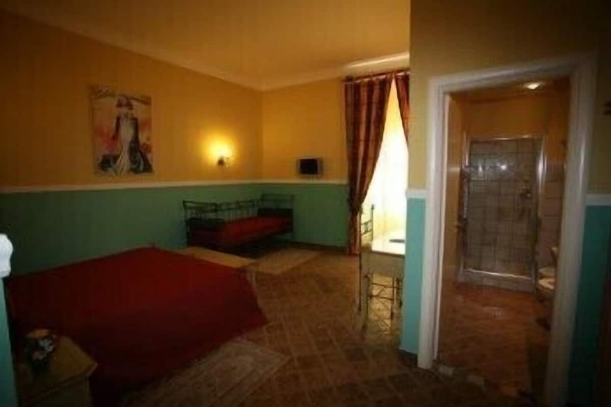 A small, dimly lit room with a bed, a table, and a shower area.