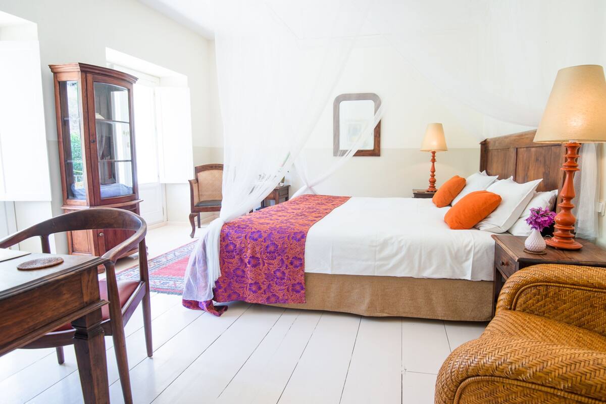 Une chambre à coucher avec un lit, des lampes de chevet, une chaise, un bureau et une fenêtre.