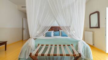 Un dormitorio con cama con dosel, un banco de madera, un espejo y un radiador.