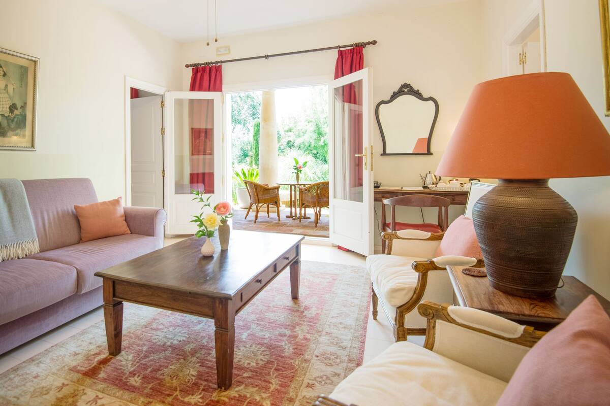 Un salon comprenant un canapé, une table basse et des fauteuils, un coin repas avec une table et des chaises, et une vue sur l’extérieur grâce à une porte ouverte.