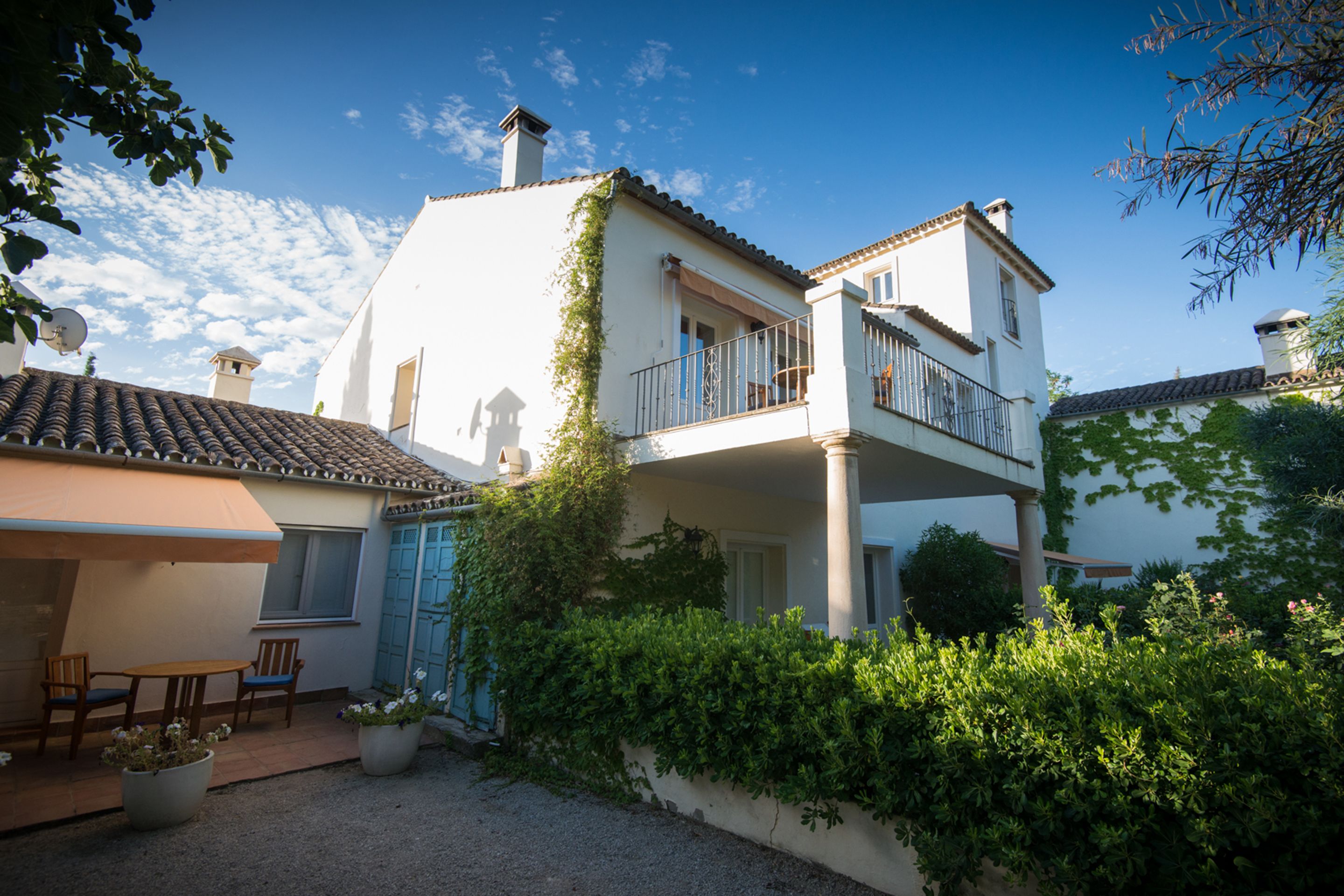 A two-story house with a balcony, a patio with chairs, and a garden area.