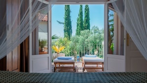 Une chambre avec un lit, deux tables de chevet et une vue sur un balcon équipé de deux chaises longues et d’une rambarde.