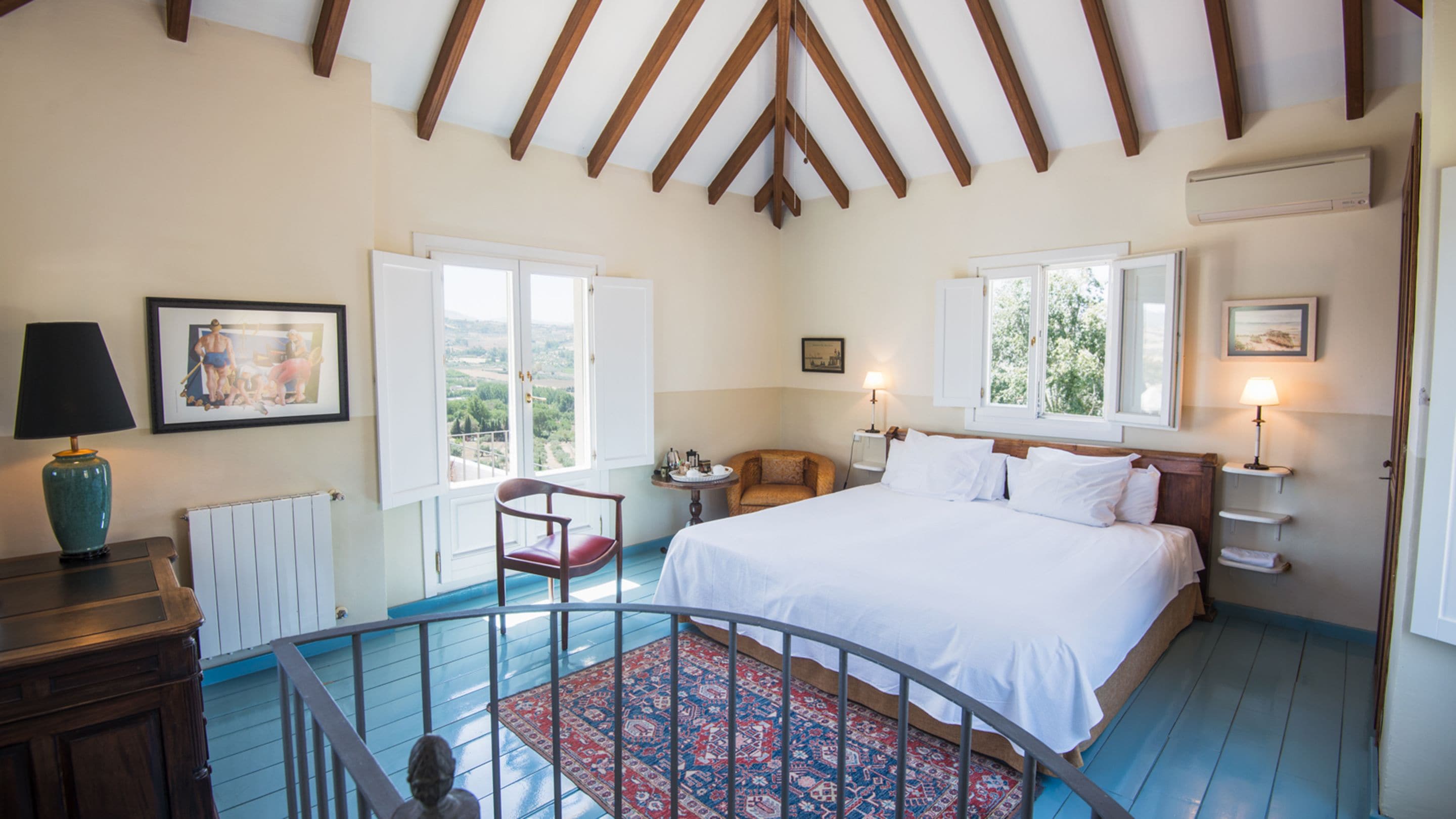 Un dormitorio con una cama grande, una silla, una mesa y vistas al exterior.