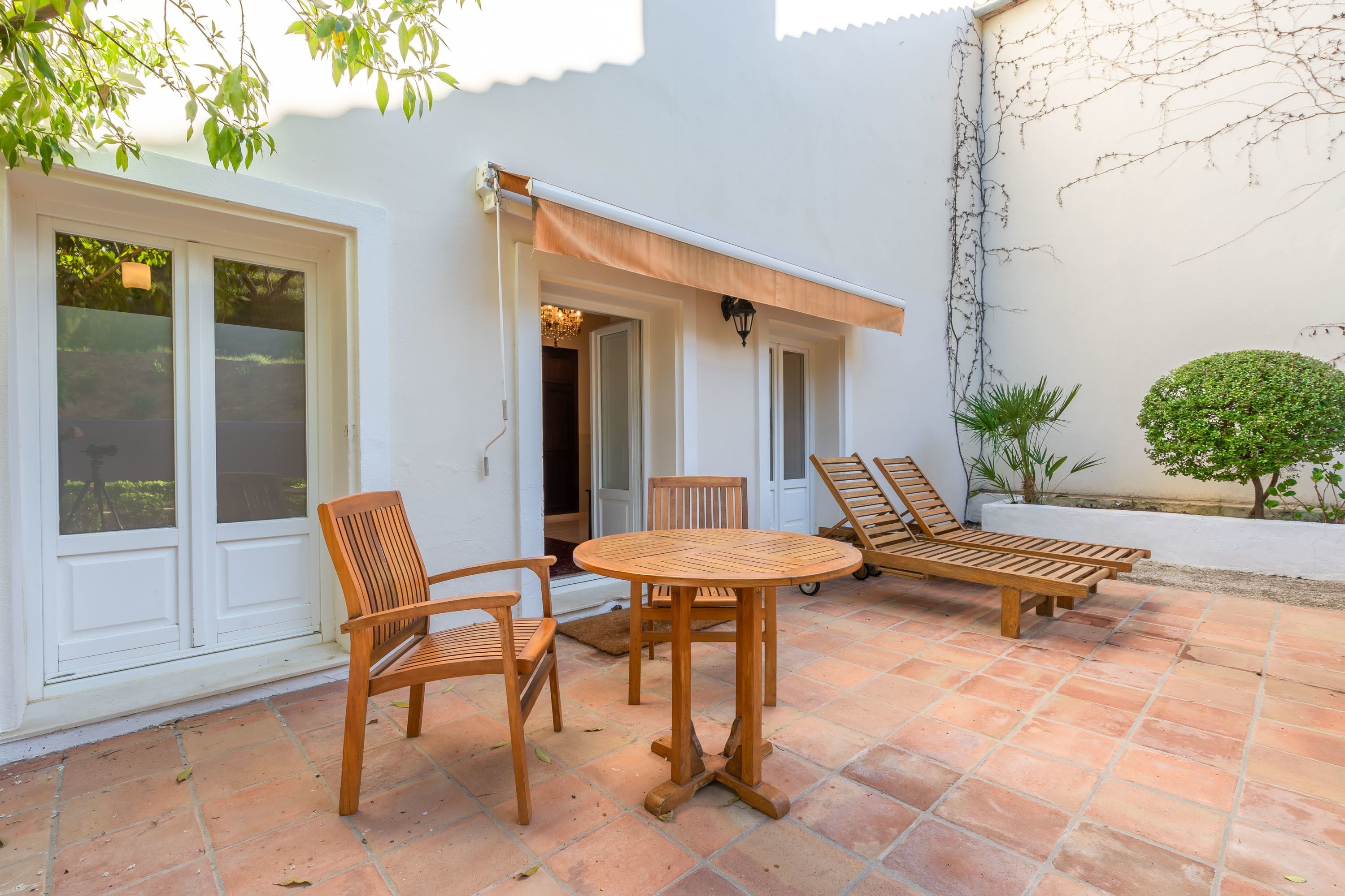 A patio with wooden furniture, a white wall, and a small garden.