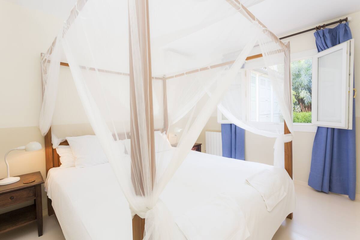 Une chambre à coucher avec un lit à baldaquin, une table de chevet avec une lampe et une fenêtre avec des rideaux.
