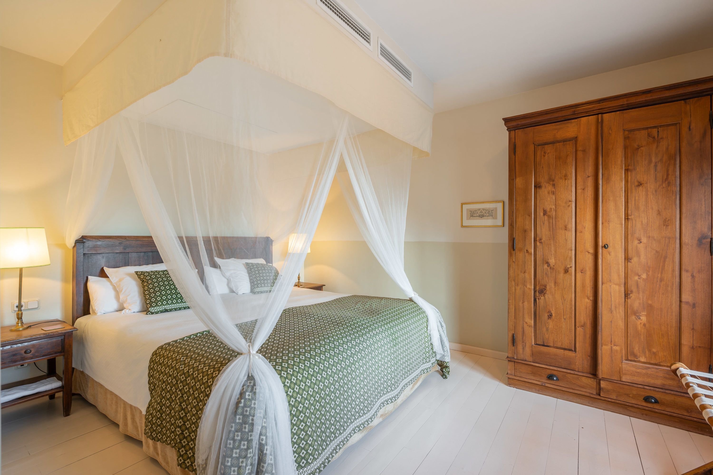 A bedroom with a four-poster bed, a wooden wardrobe, and a nightstand with a lamp.
