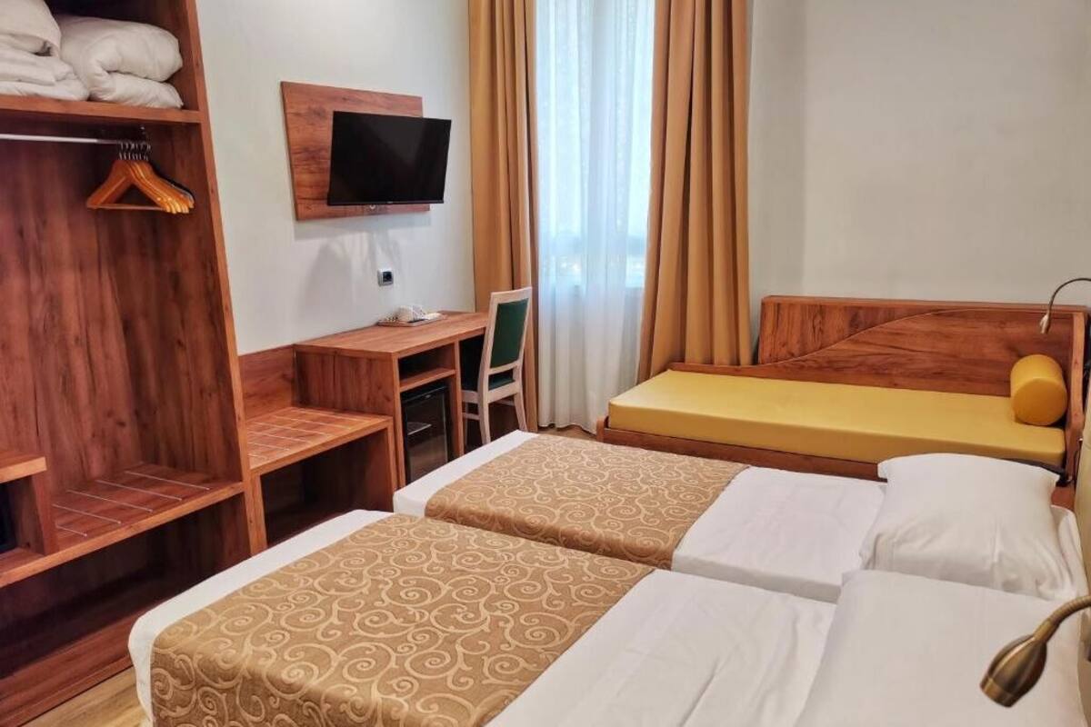 Habitación de hotel con dos camas, un escritorio con silla, un televisor montado en la pared y un armario.