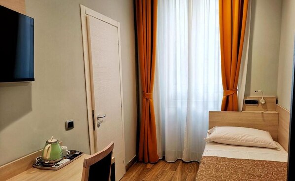 A hotel room with a bed, a TV mounted on the wall, a coffee maker on the side table, and curtains. - CSI Group - Hotel Central Station (Milan)