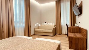A hotel room with a bed, a sofa, a wooden side table, and a TV mounted on the wall. - CSI Group - Hotel Central Station (Milan)