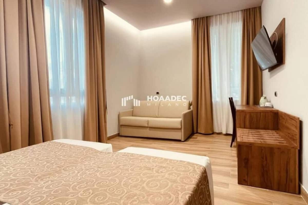 Habitación de hotel con cama, sofá, mesita de madera y televisor fijado a la pared.