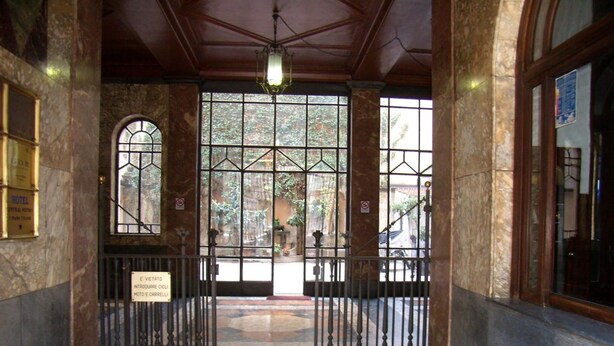 A hotel entrance with a marble floor, a sign indicating a motor and bicycle parking area, and a view of the outside through large windows. - CSI Group - Hotel Central Station (Milan)