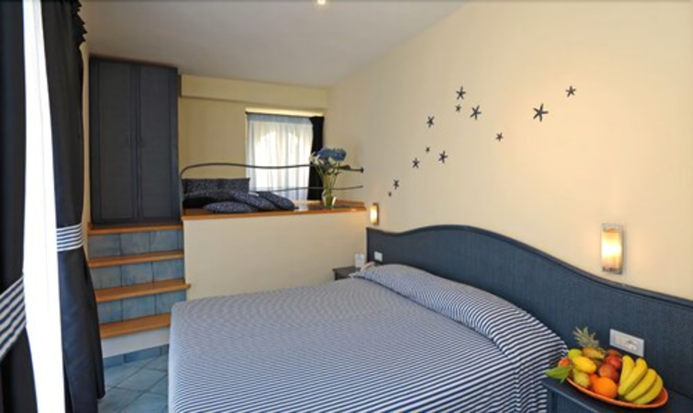 Un dormitorio con una cama, una mesita con un florero y flores, una escalera y una pared decorada con estrellas.