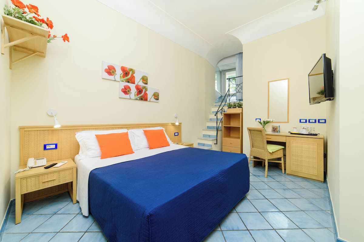 A hotel room with a bed, a desk, a chair, a television, a phone, and a plant.