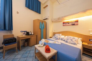 Habitación de hotel con cama, escritorio, silla, armario y una pequeña mesa con una bolsa y un libro.