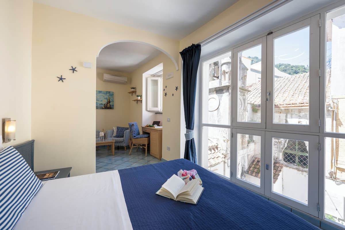 A hotel room with a bed, a desk, a chair, and a view through large windows.