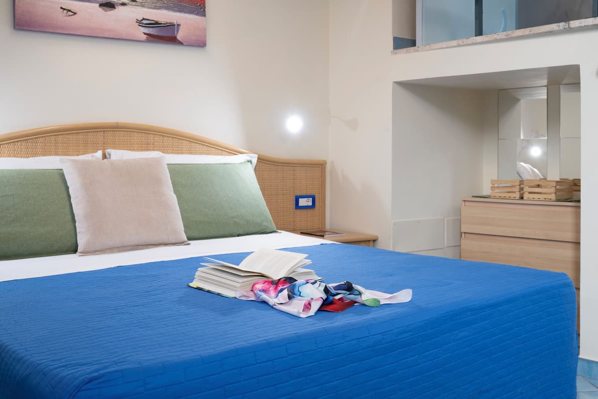 A hotel room with a bed, a nightstand, a dresser, and a painting on the wall.