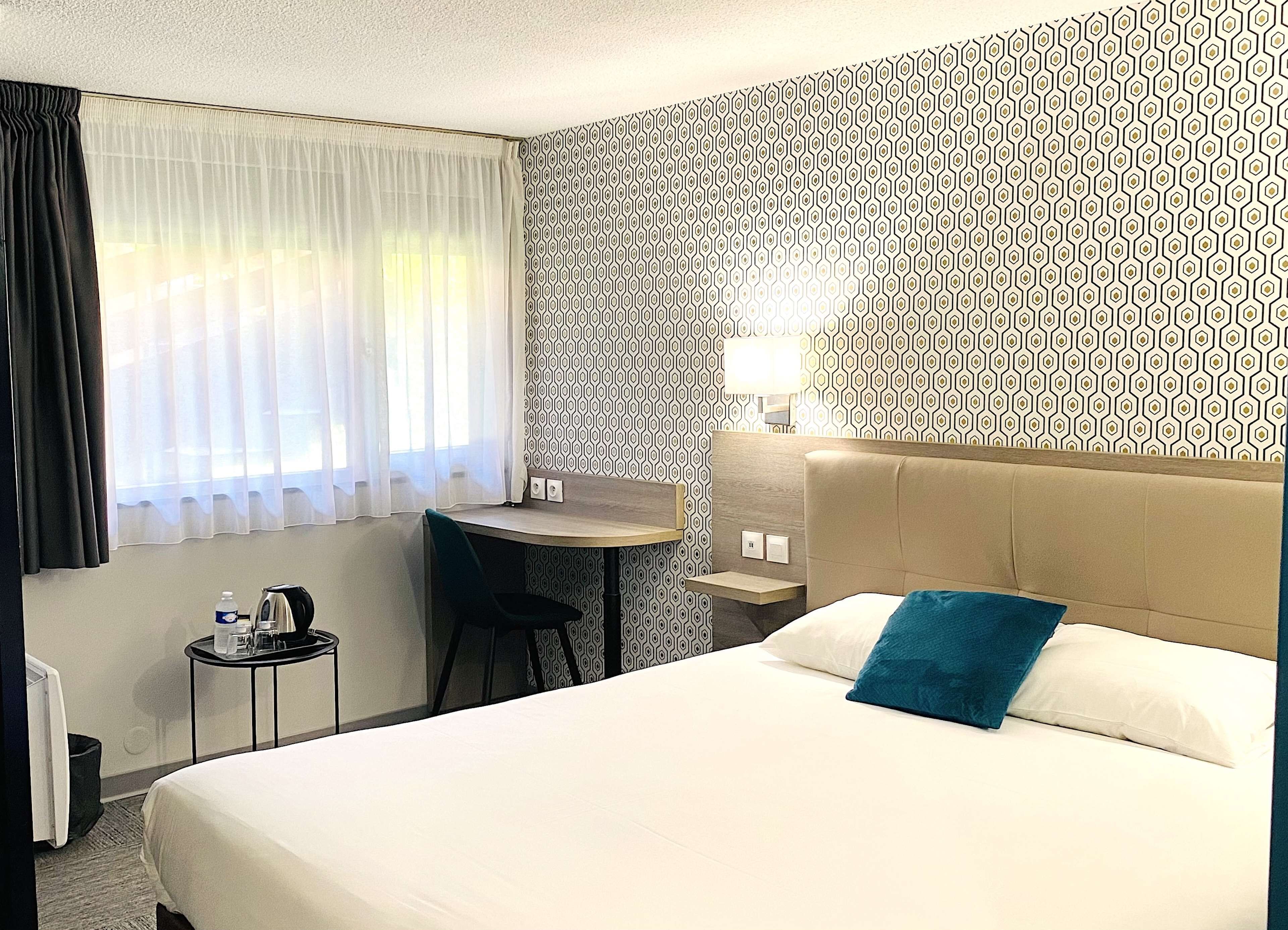 Habitación de hotel con cama, escritorio, silla y ventana con cortinas.