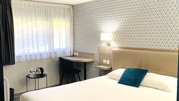 Habitación de hotel con cama, escritorio, silla y ventana con cortinas.