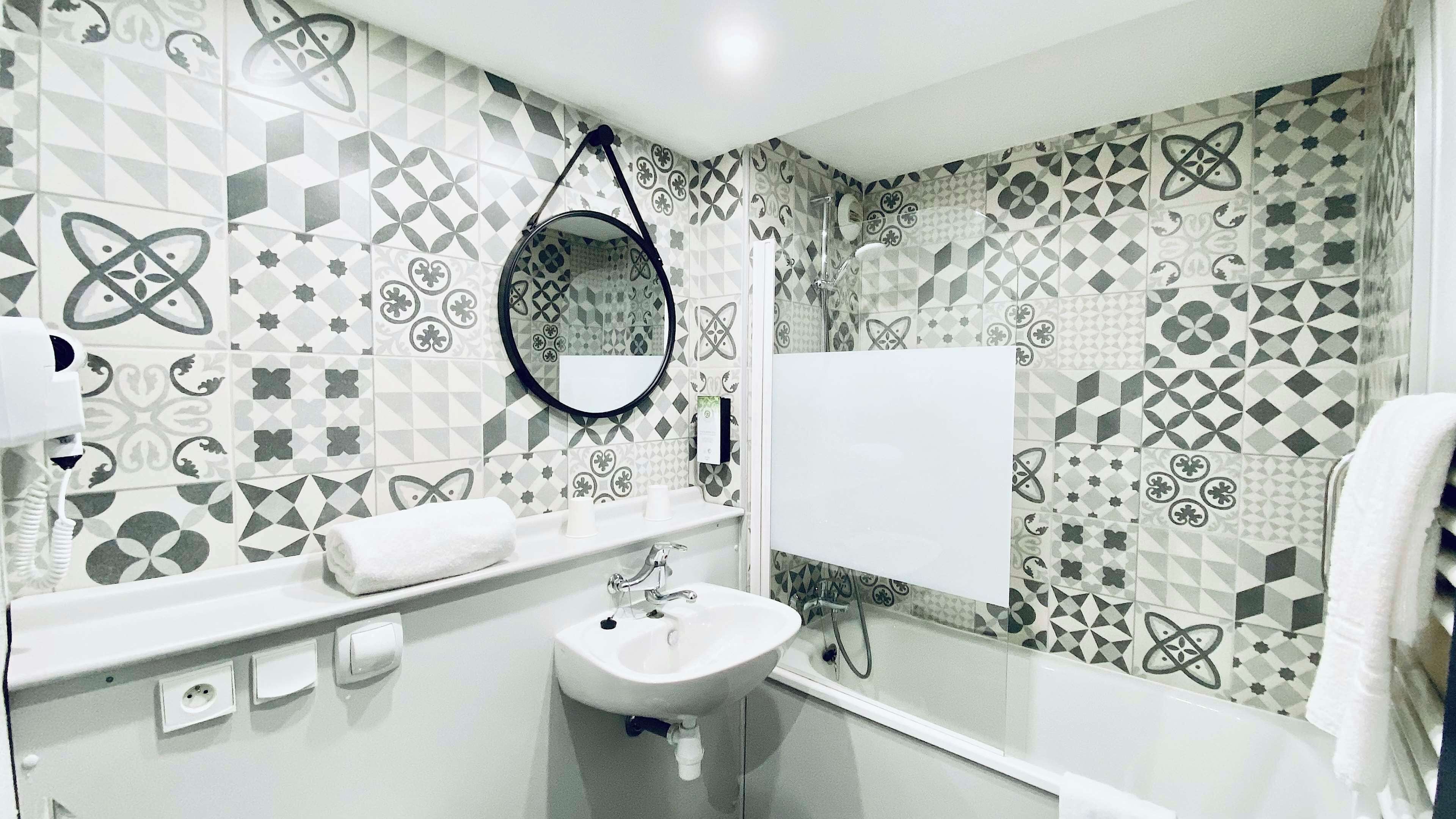 A bathroom with patterned tiles, a sink, a mirror, and a towel rack.