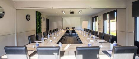 A conference room with a long table, chairs, a projector screen, and a clock on the wall.