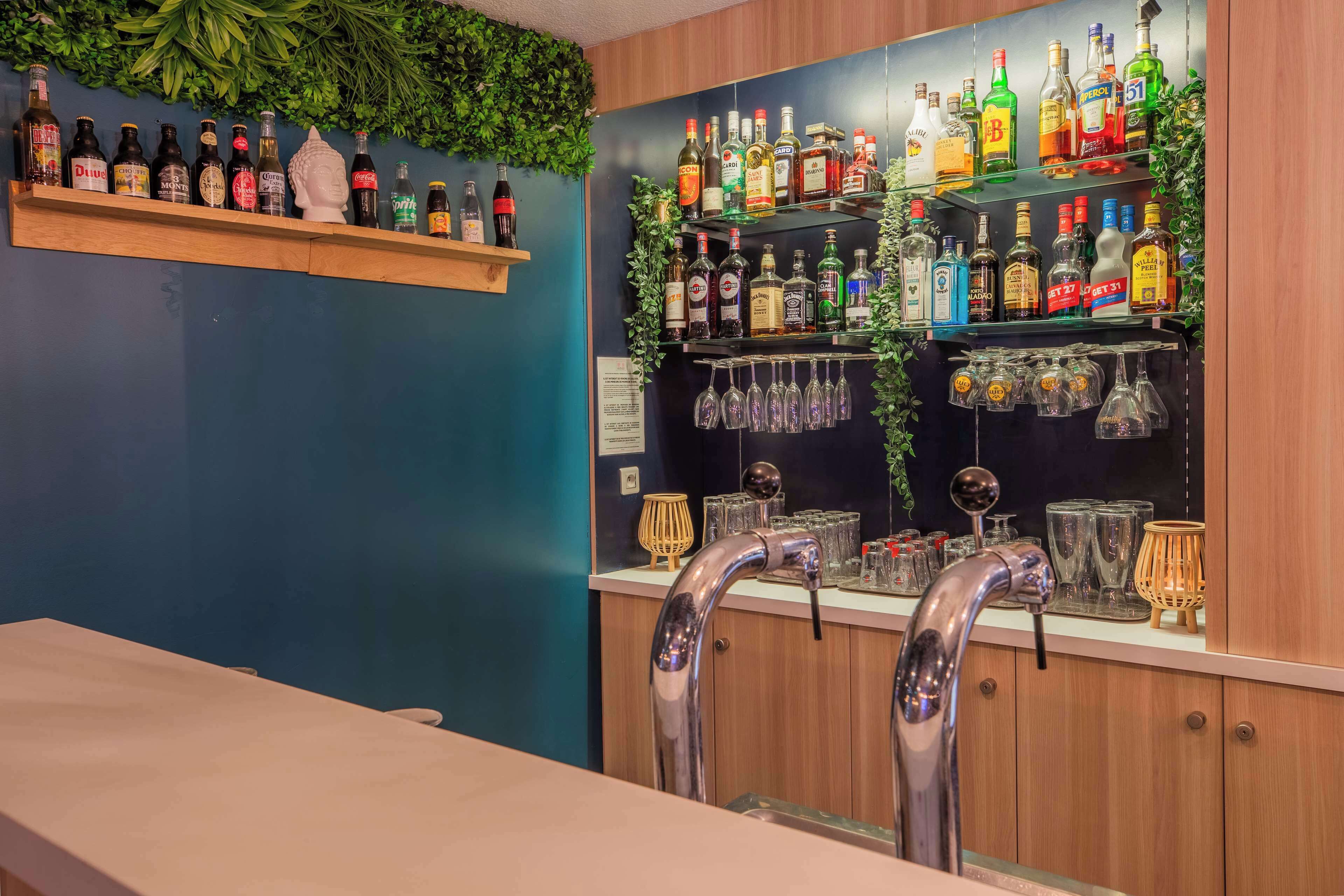 Un espace bar avec des étagères remplies de bouteilles d’alcool, un comptoir et un robinet.