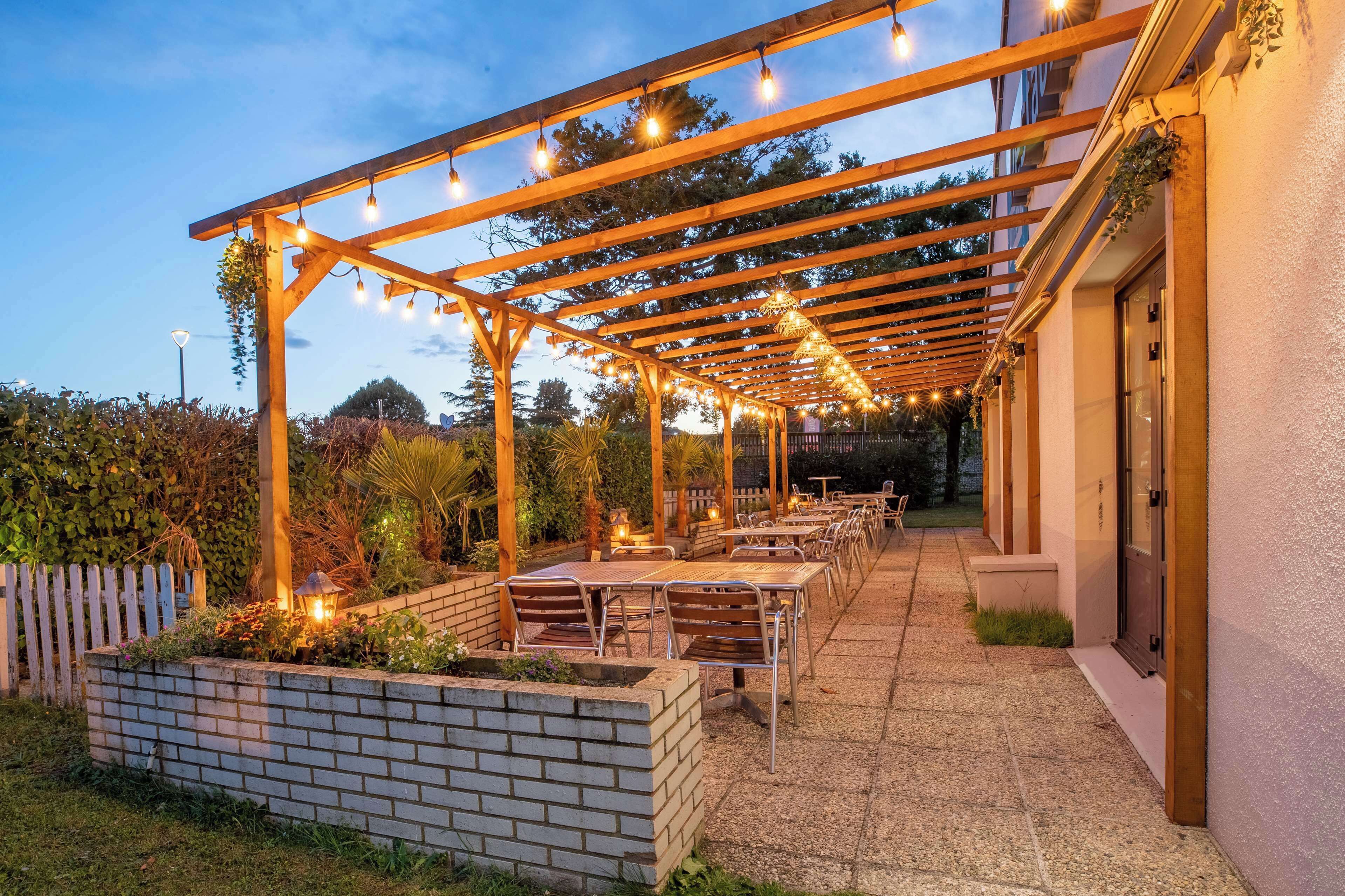 An outdoor patio with wooden pergola, string lights, and tables and chairs.