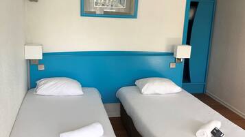 Habitación de hotel con dos camas individuales, ropa de cama blanca, cabecera azul, un cuadro en la pared y un armario azul.