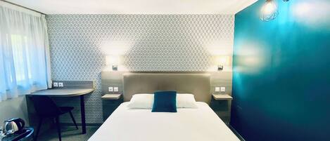 A hotel room with a bed, a desk, two bedside tables, and a chair.