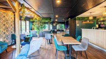 Un restaurante moderno con mesas y sillas de madera, una zona de bar y una pared verde con plantas.