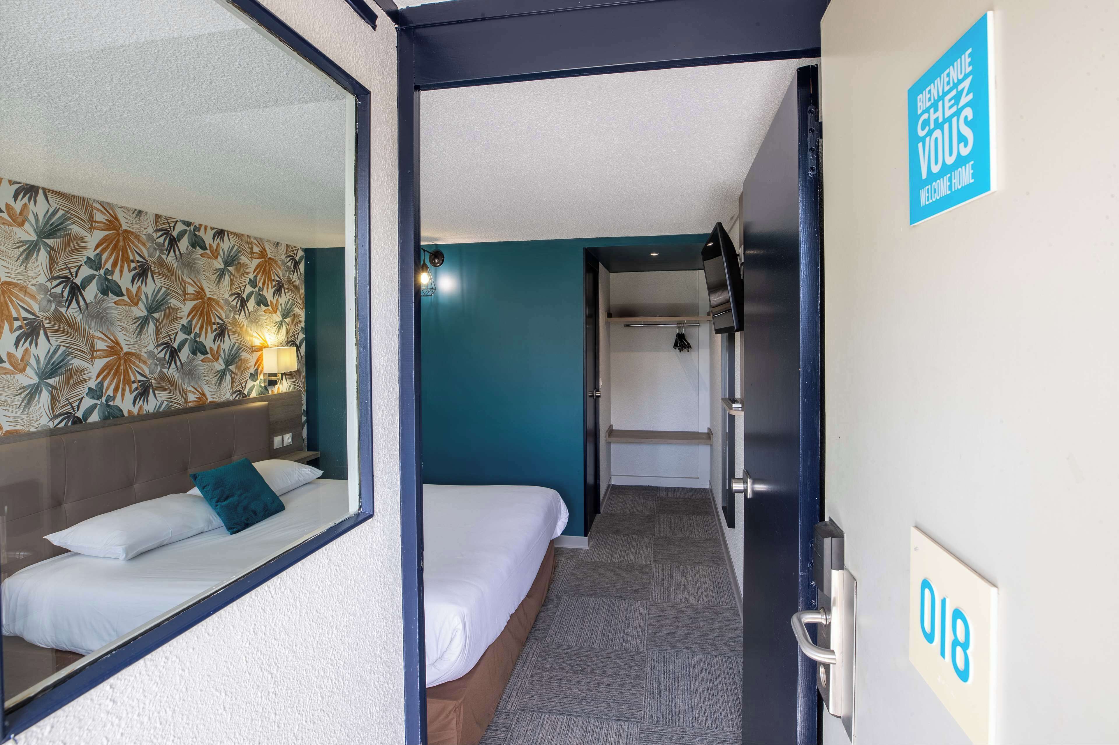 A hotel room with a bed, a wall-mounted TV, a door with a number sign, and a welcome sign.