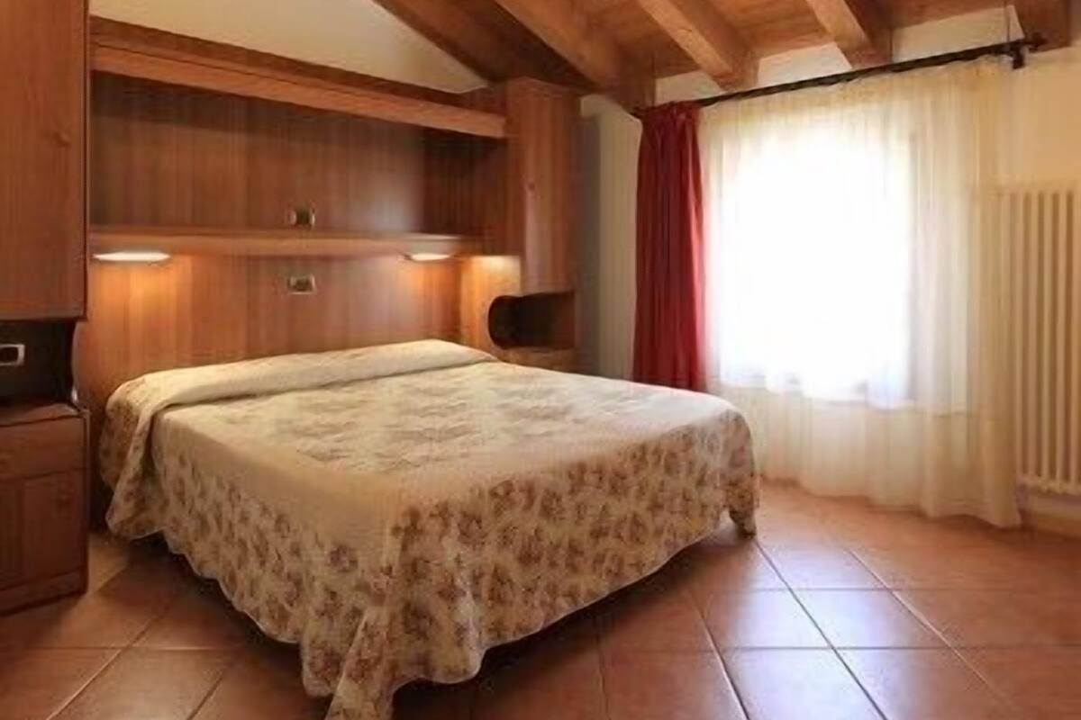 A bedroom with a wooden ceiling, a bed with a floral bedspread, and a window with curtains.