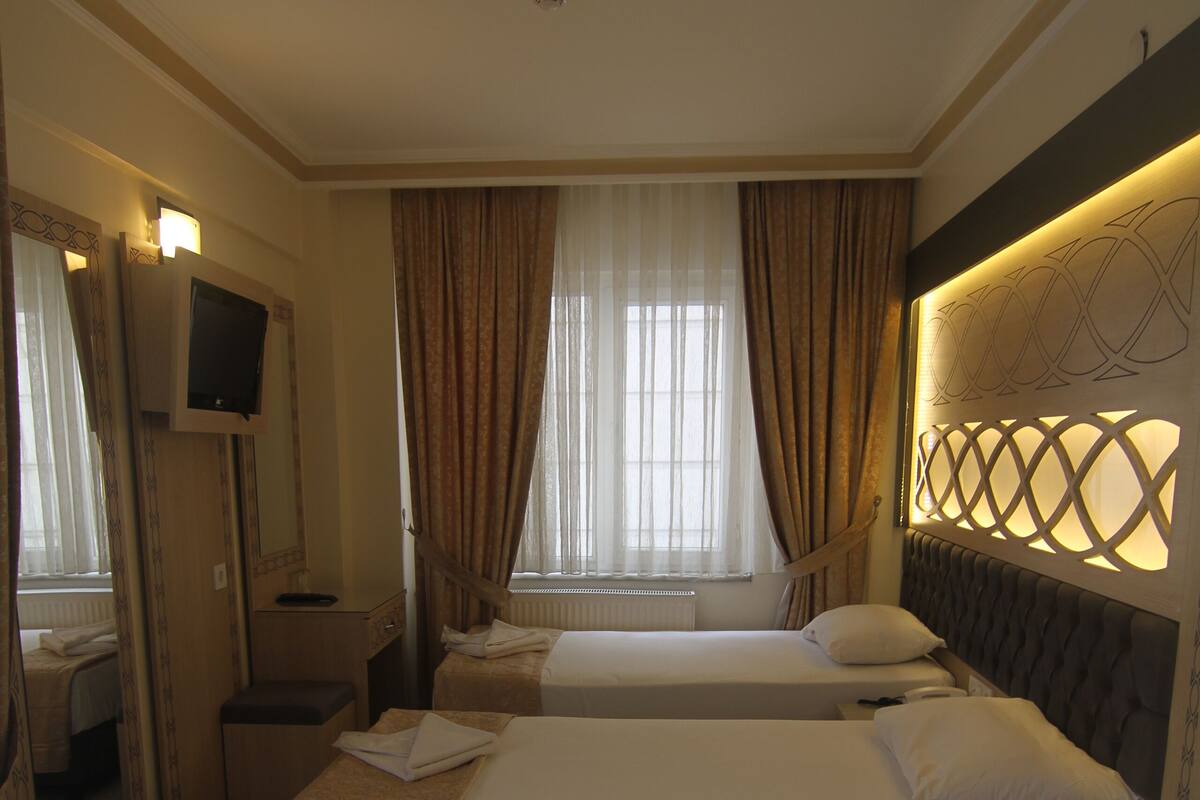 A hotel room with two beds, a TV, a mirror, and a window with curtains.