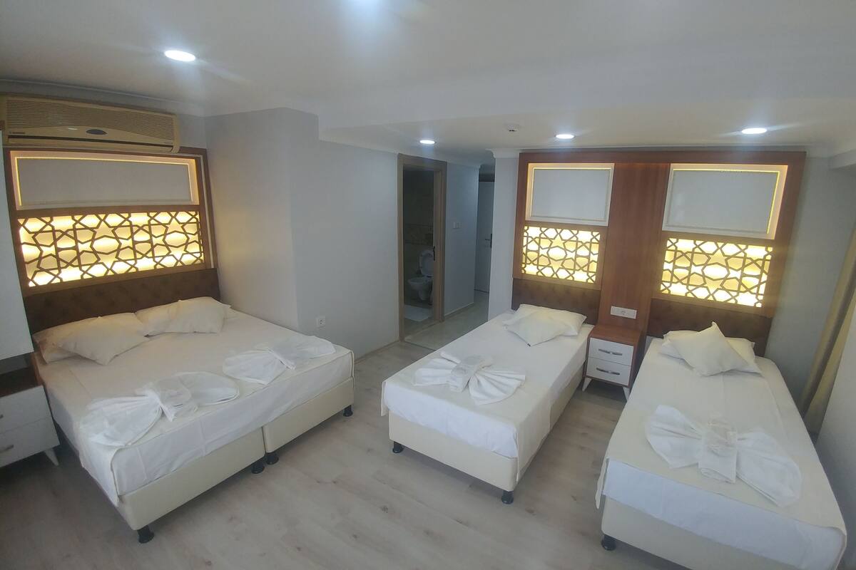 A hotel room with three beds, each with a headboard and bedside tables.