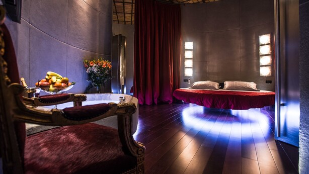 Una habitación con una cama, una silla, un frutero y un jarrón con flores.