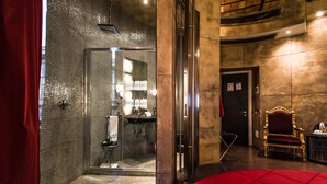 Un baño moderno con cabina de ducha de vidrio, tocador con lavamanos y una silla dorada.