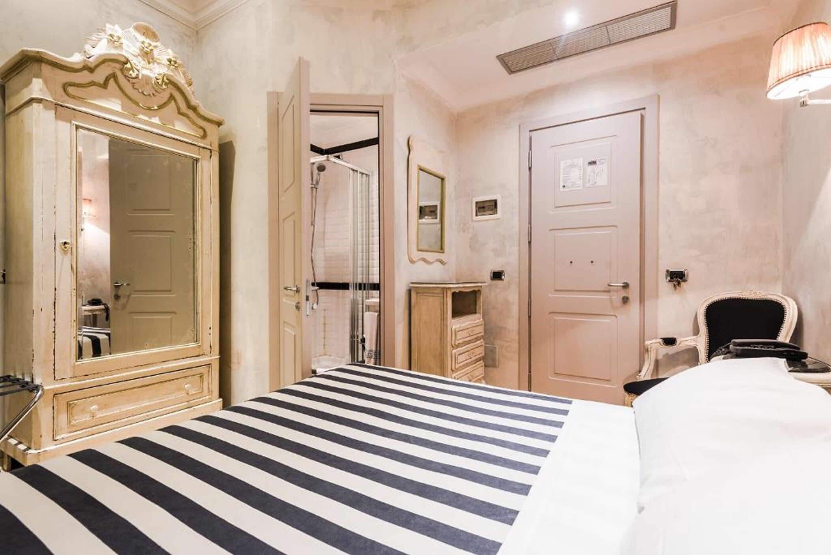 A hotel room with a striped bed, a large mirror, a wardrobe, and a shower area.