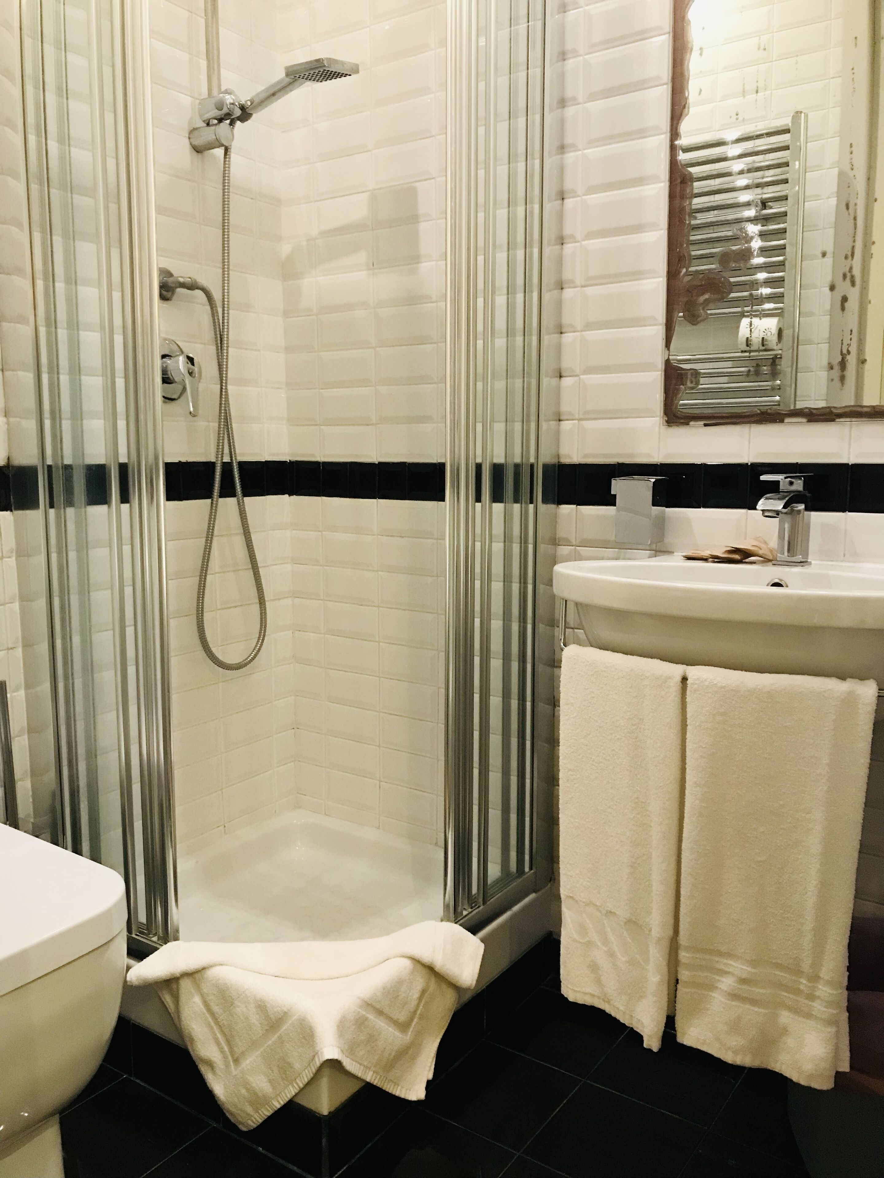 A bathroom with a glass-enclosed shower, a white sink, and two white towels.
