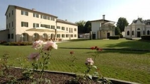 A large, multi-story building with a symmetrical facade, a well-maintained lawn, and a few blooming flowers in the foreground. - Villa Toderini Agriturismo (Codogne)