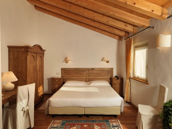 A bedroom with a wooden headboard, two bedside lamps, a large bed, a wooden wardrobe, a chair, and a window with curtains. - Villa Toderini Agriturismo (Codogne)