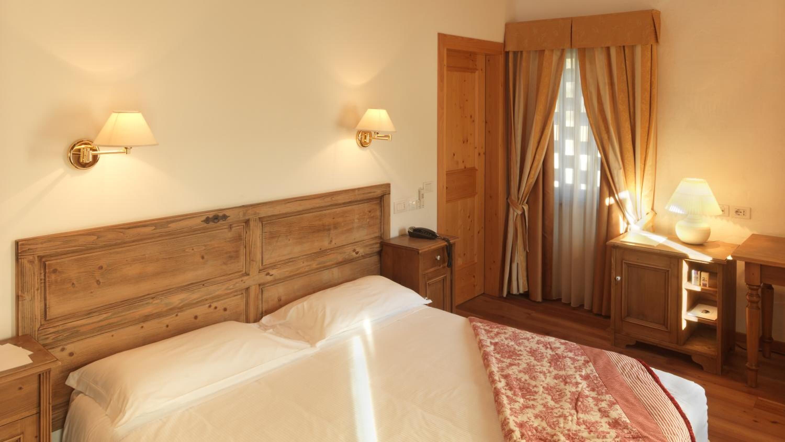 A wooden bed with two bedside lamps, a wooden wardrobe, and a window with curtains.