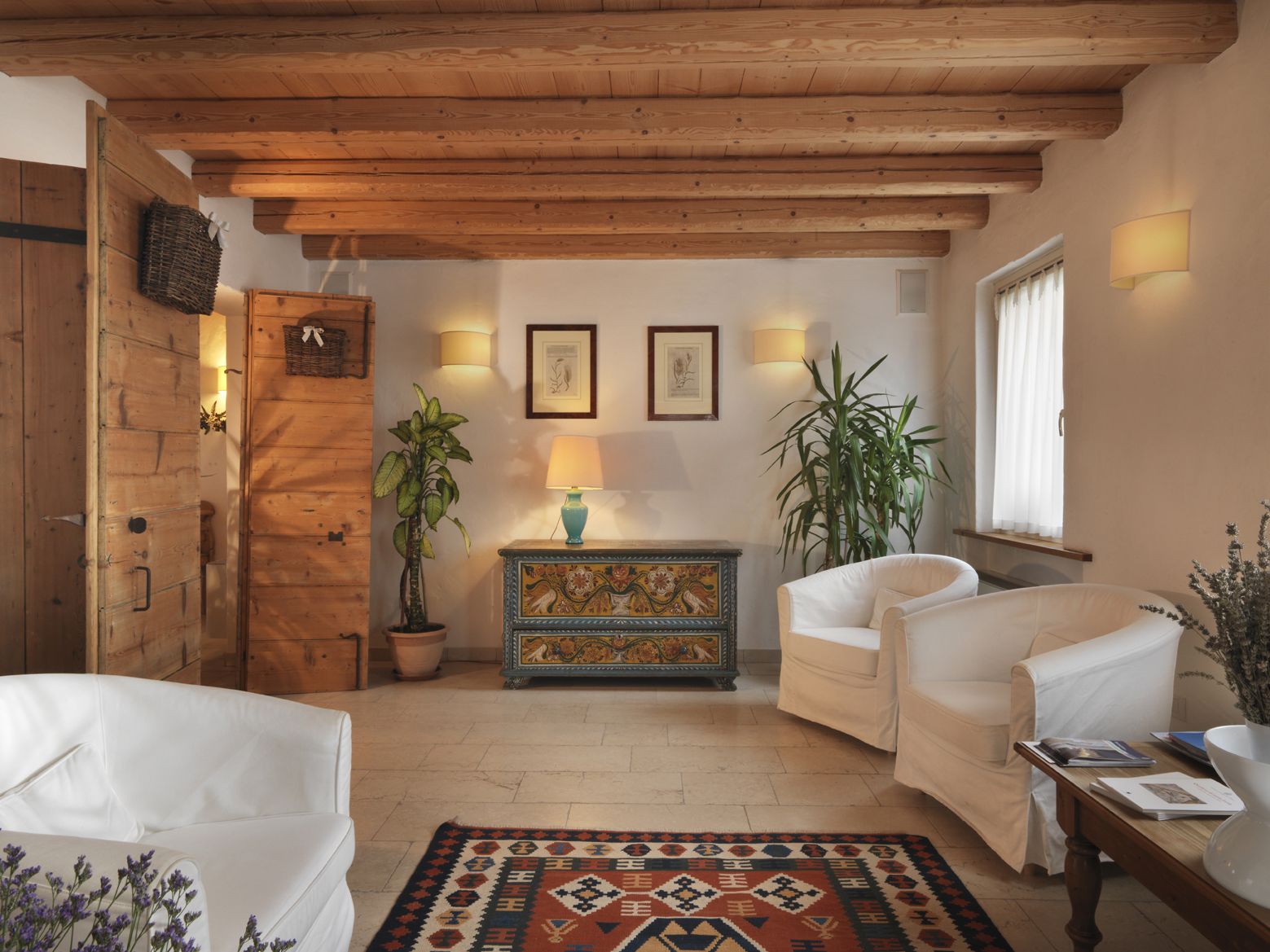 Ein gemütliches Wohnzimmer mit Holzbalken, weißen Möbeln, einem gemusterten Teppich und Wandleuchten.