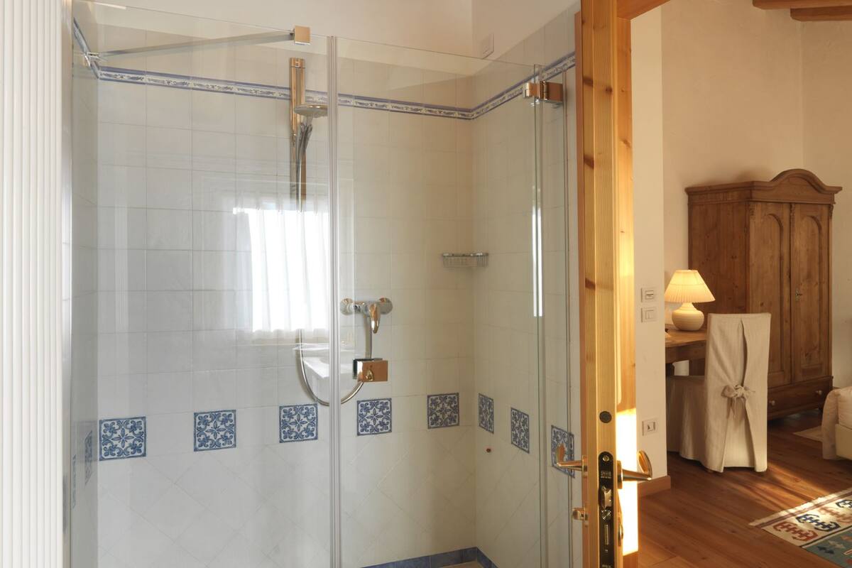 Ducha envuelta en vidrio, con ducha y panel de control, paredes de azulejos decorativos azules y piso de madera.