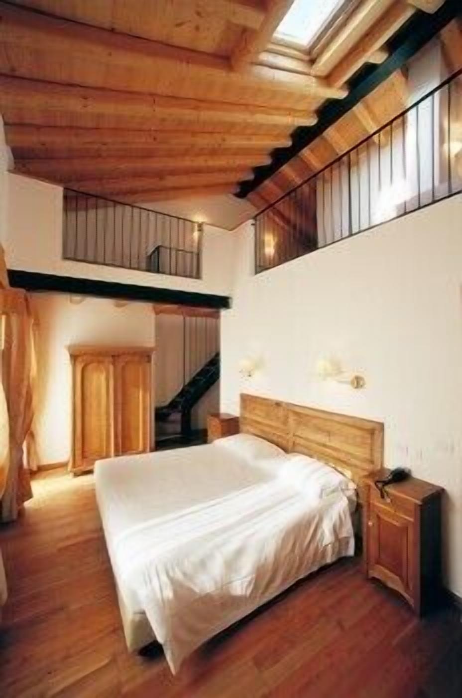 Quarto com cama grande, vigas de madeira no teto, uma escada e vista pela janela.