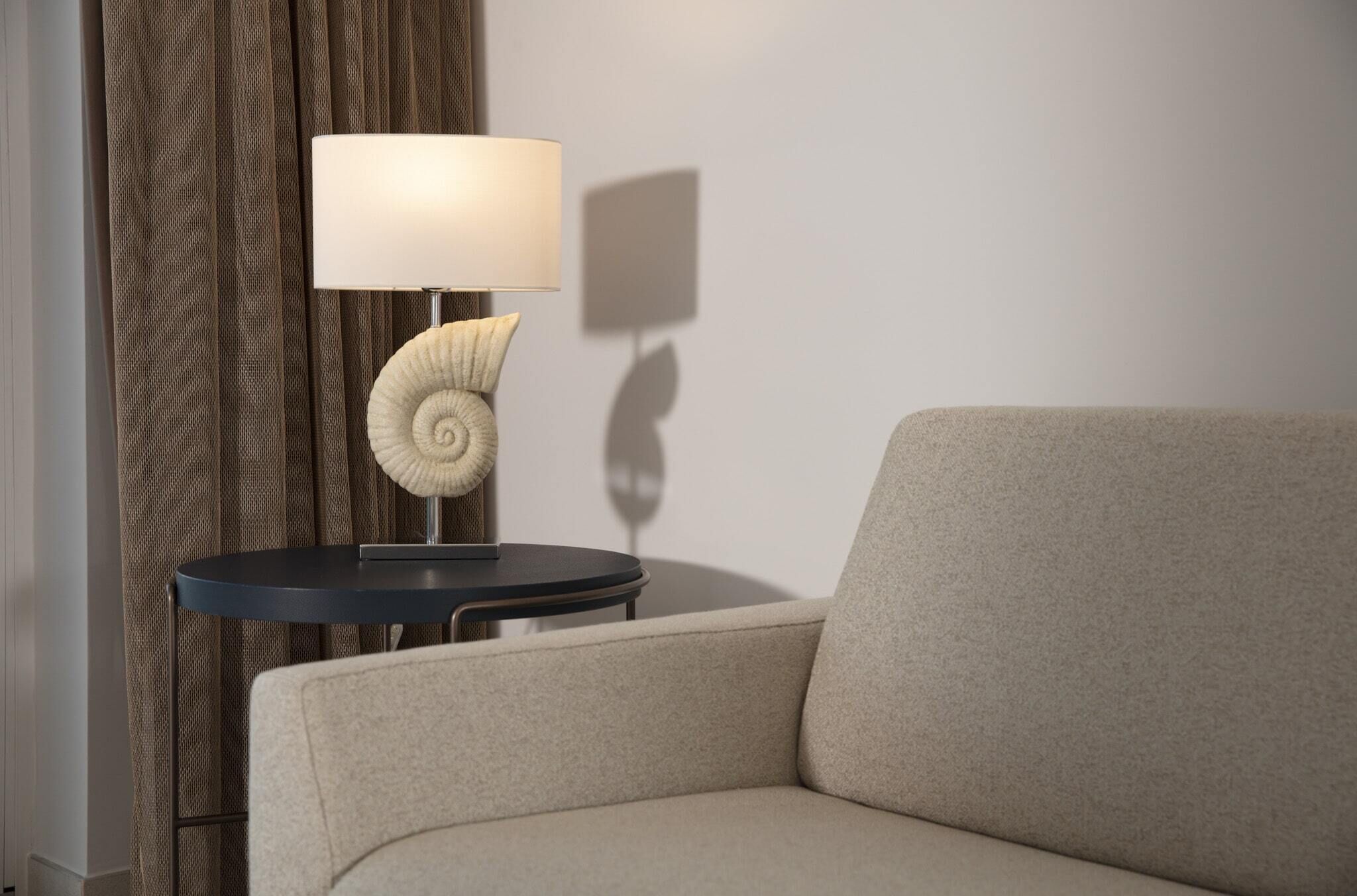 A modern room with a sofa, a round table with a lamp, and a curtain.