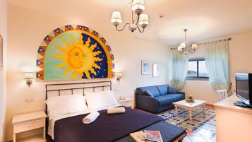 Habitación de hotel con cama, escritorio, silla, televisor y un mural grande con motivos de sol en la pared.