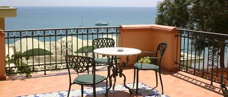 A terrace with a table and chairs, a view of the sea, and a tiled floor.